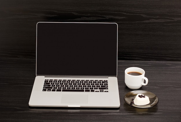 Откройте ноутбук, кружку кофе и панна котту на черном деревянном столе, обеденный перерыв