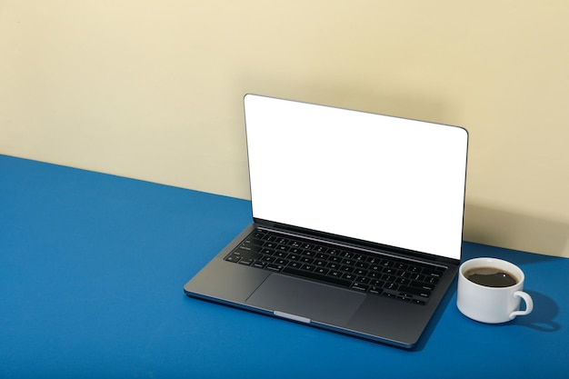Open laptop with blank screen and cup of coffee on blue table