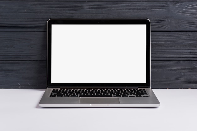 Photo an open laptop with blank white screen on white desk against black wooden backdrop