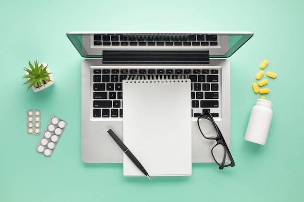 Open laptop with pills and diary on green surface