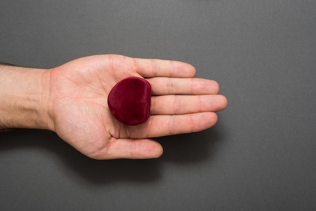 Open male palm with a red heart-shaped jewelry box. Present. Black background