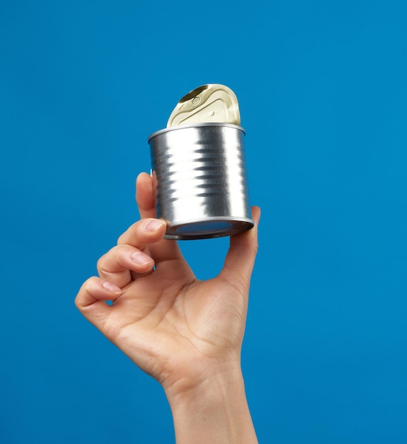 Photo open metal round tin can in a female hand on a blue background close up