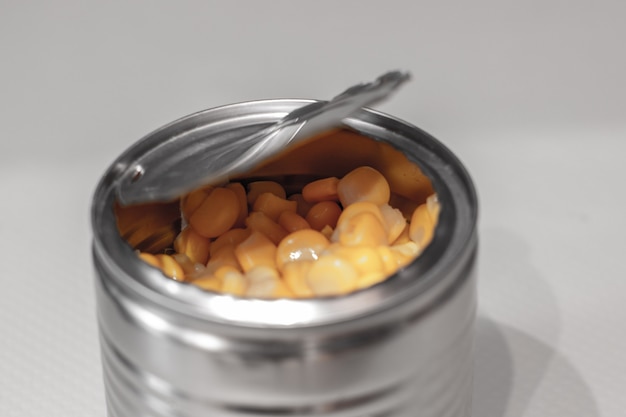 Open metallic can with sweet corn on a white.