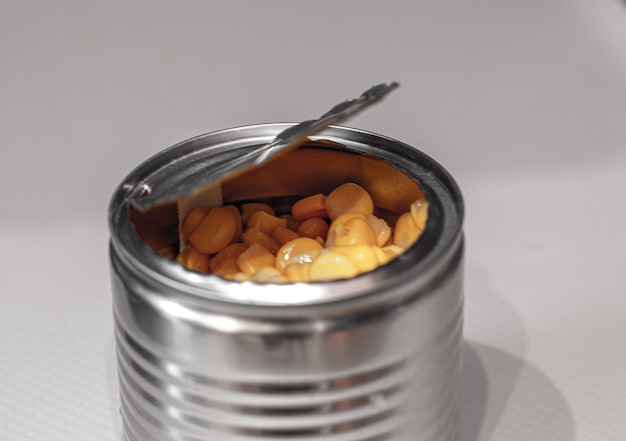 Open metallic can with sweet corn on a white.