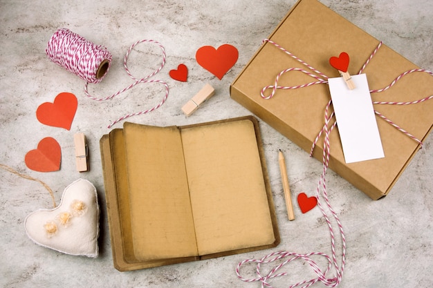   open noteboock with old vintage paper, pencil, gift box with blank white label, hearts on a marble