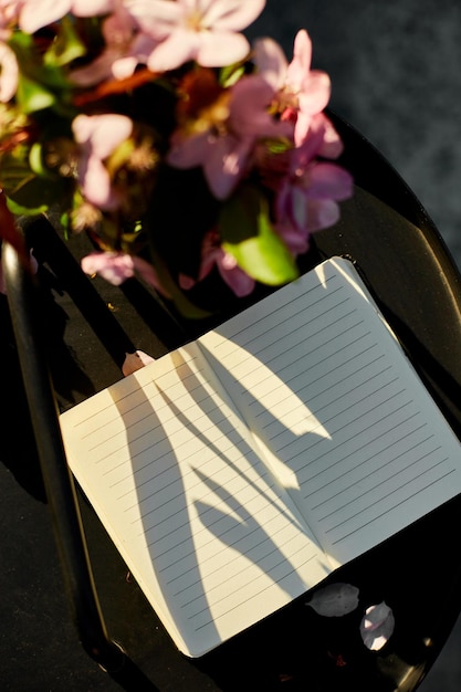 写真 開いたノートブックと花とテラス上の小さな黒いテーブルで 晴れた日にハードライトの屋外ワークスペース 夏のリラックスノート アイデアプランニング