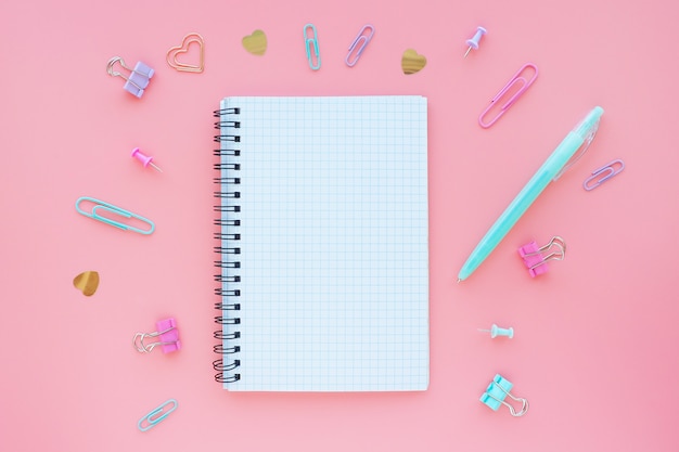 Open notebook in a box on a spring on a pink background and stationery around. Space for text. Flat layout.
