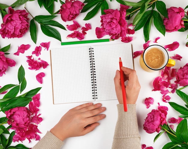 Open notebook in a cage and two female hands, a yellow cup with coffee 