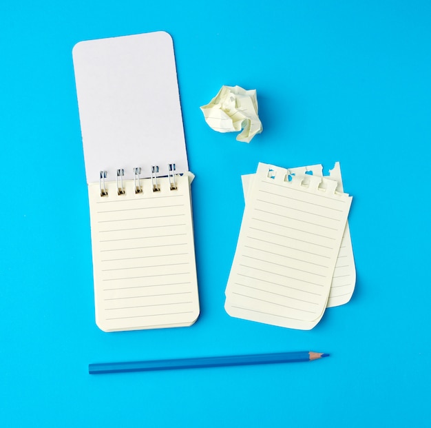 Photo open notebook in line and a blue wooden pencil, next to torn and wrinkled pages