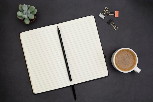 Open notebook with empty page and coffee cup. Table top, work space on dark background. Creative flat lay.