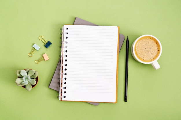 Open notebook with empty page and coffee cup. table top, work\
space on green background. creative flat lay.