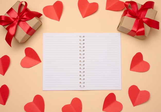 Open notebook with empty white sheets red hearts and gift boxes on a beige background