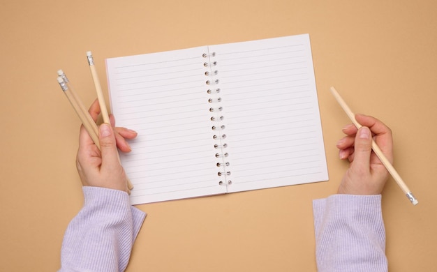 Open notebook with empty white sheets and a womans hand holding a wooden pen on a yellow background