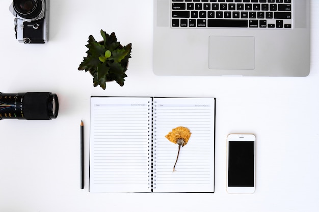 Apra il taccuino con le pagine in bianco del fiore, il computer portatile, la macchina fotografica, l'obiettivo