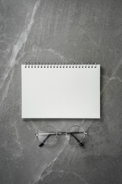 Open notebook with glasses on grey marble table top view, spiral notepad on gray office desktop. clear to do list, flat lay.