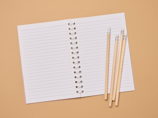 Open notebook and wooden pencils on brown background