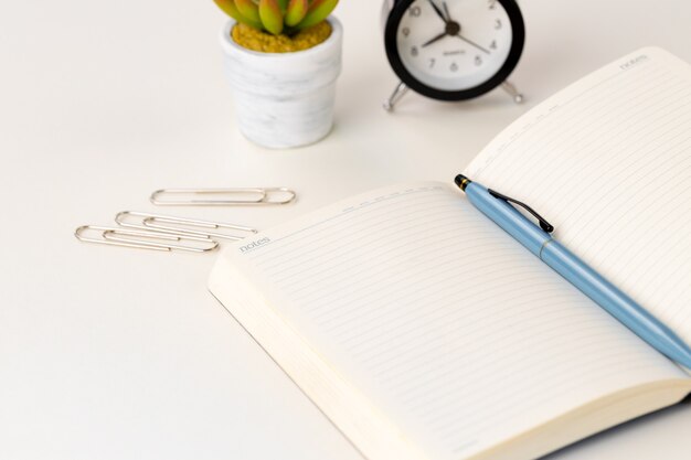 Open notepad, alarm clock and succulent on working table