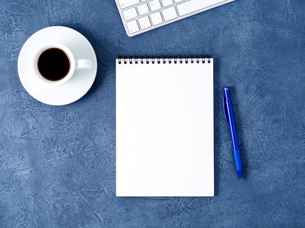 세 어두운 파란색 돌 테이블에 열린 메모장 깨끗한 흰색 페이지, 펜 및 커피 컵, 평면도