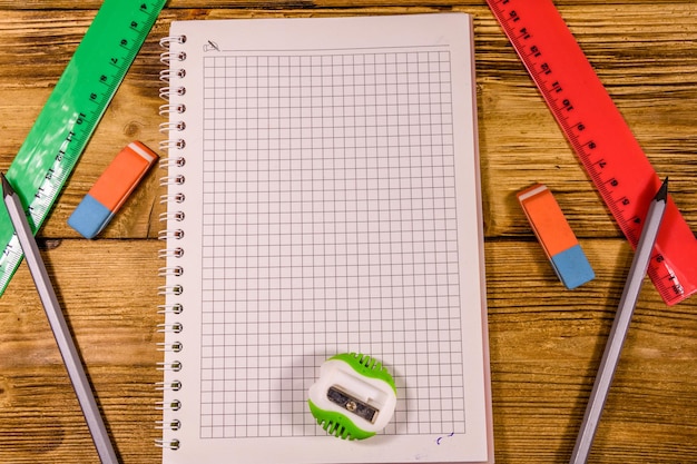 Open notepad and different stationeries on a wooden table Top view