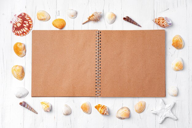 Open notepad with sea shells on white wood