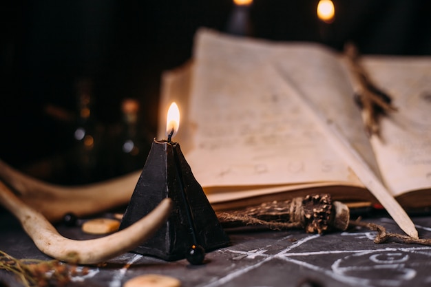 Open old book with magic spells, runes, black candles on witch table. Occult, esoteric, divination and wicca concept. Halloween scene