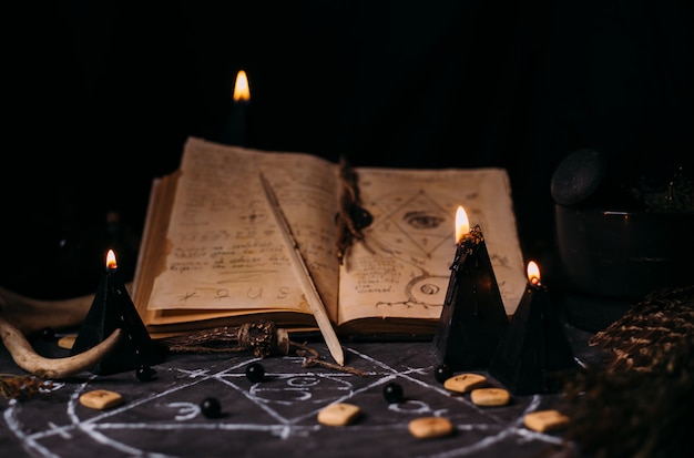 Open old book with magic spells, runes, black candles on witch table. Occult, esoteric, divination and wicca concept. Halloween scene