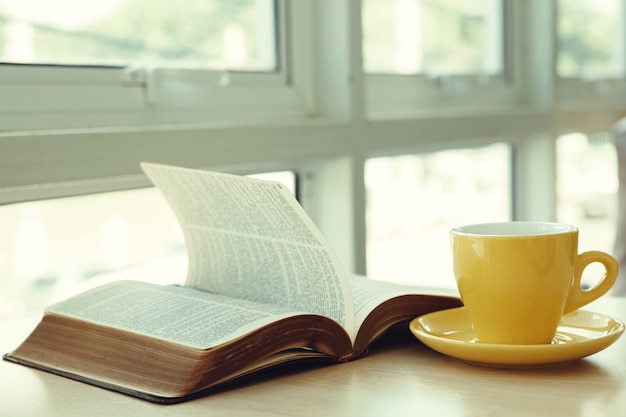 Open old book with yellow cup of coffee on the desk