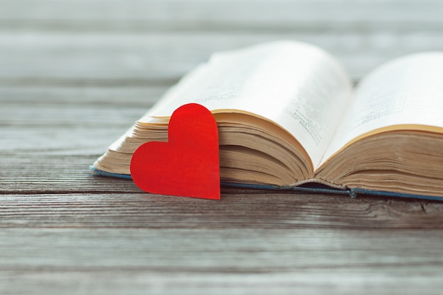 Open oud boek en rood papier hart op houten tafel