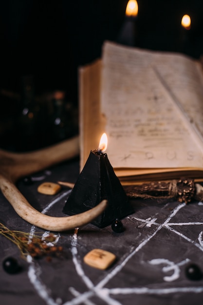 Open oud boek met magische spreuken, runen, zwarte kaarsen op heks tafel. Occult, esoterisch, waarzeggerij en wicca-concept. Halloween scène