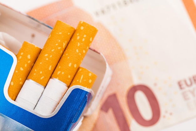 Open pack of cigarettes with yellow filter on the background of Euro banknotes