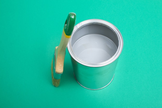 Open paint can with brush beside