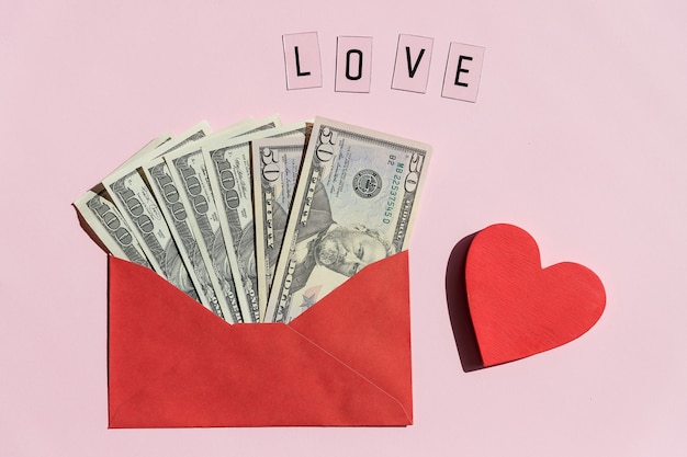 Open a paper envelope with the hundred dollar bills, isolated on pink surface.Banknotes folded in an envelope as a present. Sending or saving money, corruption concept.Cash bills for gifts