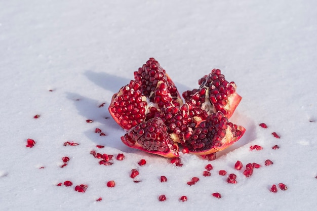 Open pomegranate fruit with red seeds on a white snow in winter close up