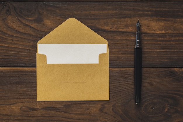 An open postal envelope with a sheet of paper and a fountain pen on a wooden background. Flat lay.