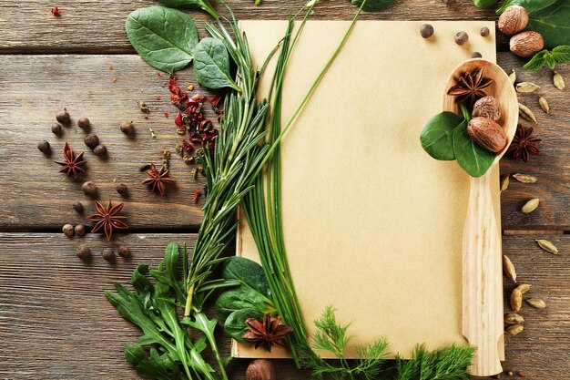 Open recipe book with fresh herbs and spices on wooden background