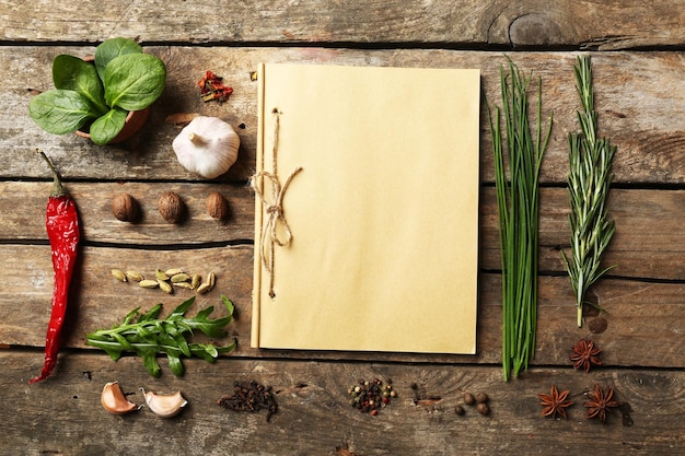 Open recipe book with fresh herbs and spices on wooden background