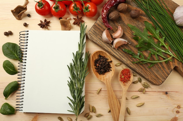 Open recipe book with fresh herbs tomatoes and spices on wooden background