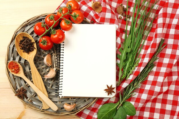 Open recipe book with fresh herbs tomatoes and spices on wooden background