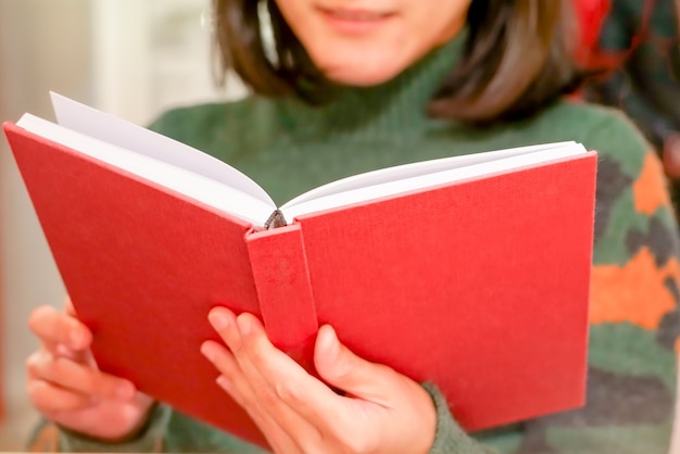 開いている赤い本は、女性の手を自宅で持っている/読んでいる