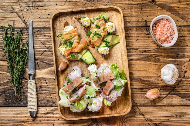 Open sandwich with  salmon and herring, cream cheese and salad on a cutting board.