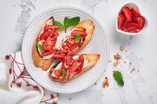 Open sandwiches met aardbeien, zachte kaasmunt en walnoot in keramische plaat op een lichtgrijze stenen ondergrond. zomer en gezond dieet, vegetarisch voedselconcept. bovenaanzicht.