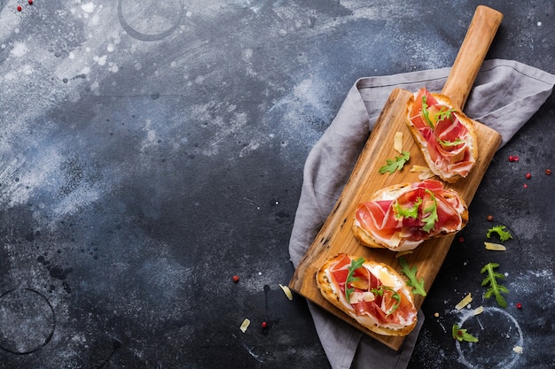 Open sandwiches with jamon, arugula and hard cheese on a concrete old dark surface