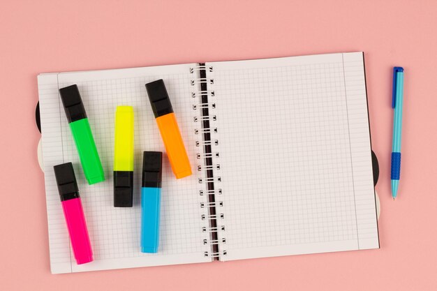 사진 핑크색 배경에 분홍색 펜과 컬러 마커를 가진 사각형 노트북을 열고 빈 색 시트를 사용합니다.