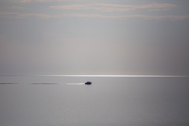 Открытое море. Вдали плывет лодка. Небо почти сливается с водой. Лодочная тропа параллельна горизонту. Есть место для копирования.