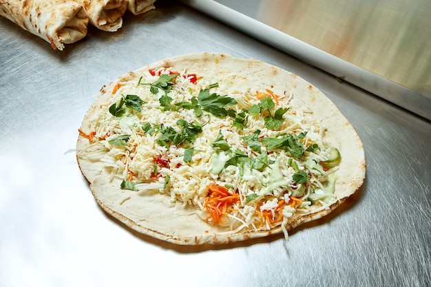 금속 표면에 치즈, 야채, 양배추, 허브 및 흰색 피타 소스로 shawarma를 엽니 다. 맛있는 길거리 음식 케밥