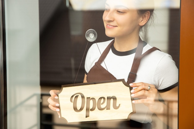 Open sign on the glass with reflection of street cafe or restaurant. Coronavirus pandemic new safety rules. Opening after quarantine time. Small business recovery after insulation. Close up.