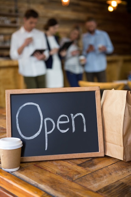 Photo open signboard with disposable coffee cup and paper bag on table in cafeteria