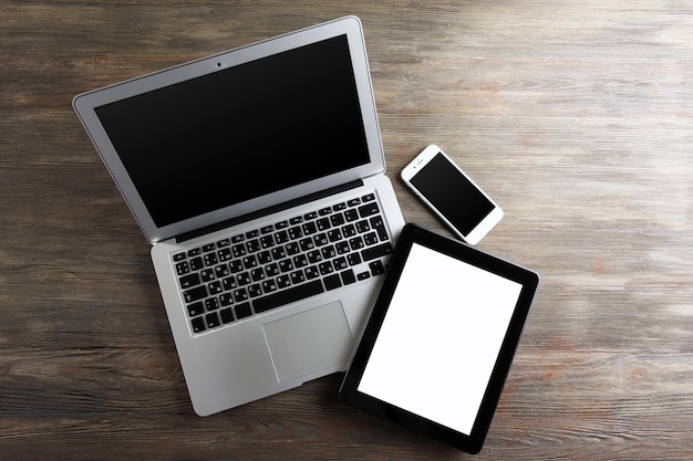 An open silver laptop mobile phone and modern tablet on the wooden background