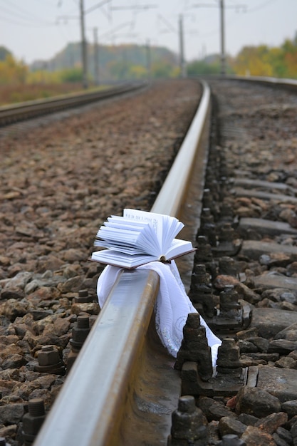 Photo open a small book lies on a white shawl on the tracks on a cloudy day