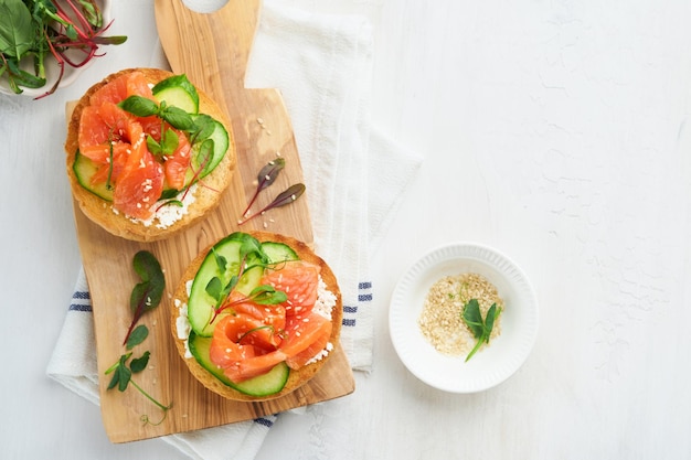 Open smoked salmon sandwiches with cream cheese cucumber sesame seeds microgreens spinach and peas leaves on light old wooden background Healthy breakfast food Delicious snack Top view